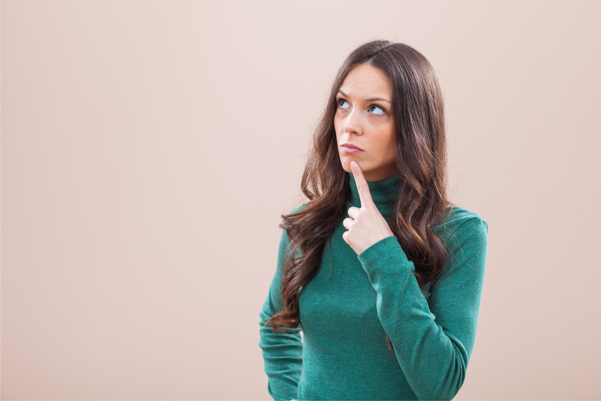 A woman in a green sweater is holding her finger to her chin and looking up.