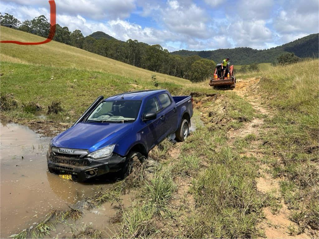 A Blue Truck Is Stuck in The Mud on A Dirt Road — Twin Lakes Towing & Recovery in Hexham, NSW