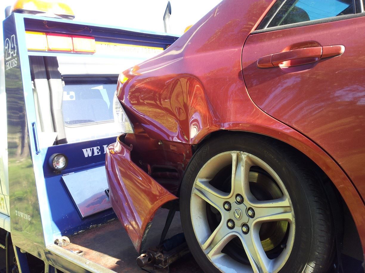 A Red Car Is Being Towed by A Tow Truck — Twin Lakes Towing & Recovery in Sandgate, NSW
