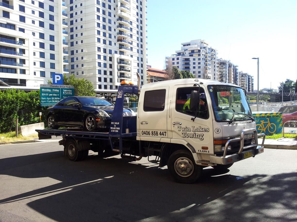 A Tow Truck Is Carrying a Black Car on The Back of It — Twin Lakes Towing & Recovery in Hamlyn Terrace, NSW