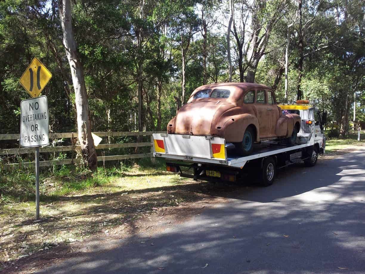 An Old Car Is Being Towed Down a Road by A Tow Truck — Twin Lakes Towing & Recovery in Hamlyn Terrace, NSW