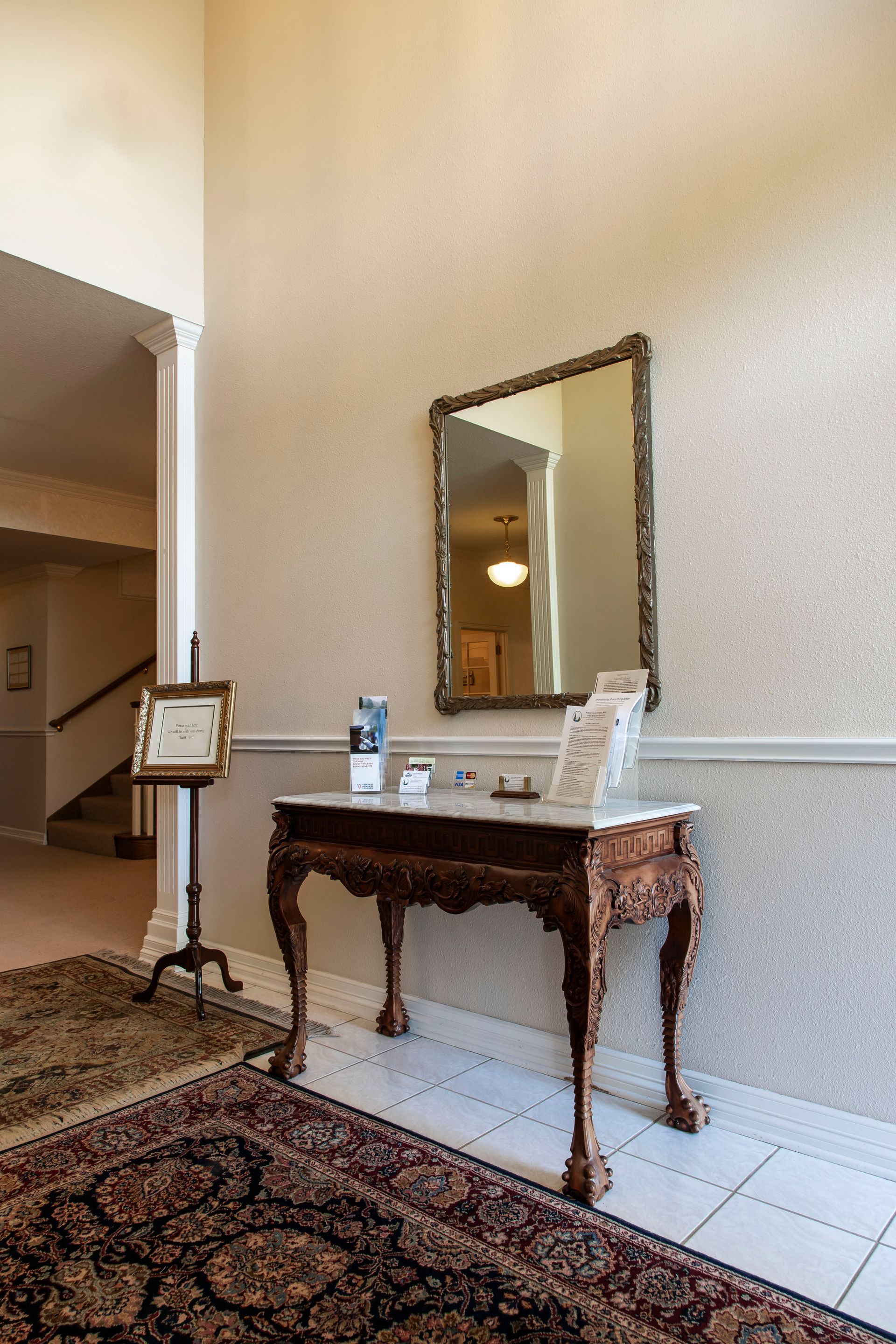 Entryway with ornate table, mirror, and brochures. Staircase and rug visible.
