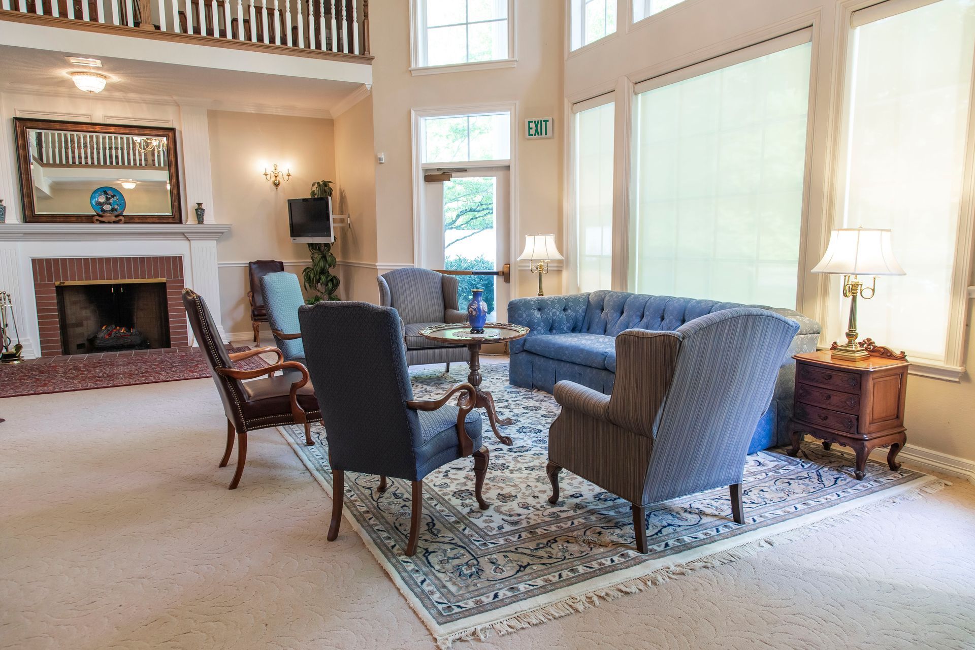 Cozy living room with fireplace, blue sofa, armchairs, rug, and tall windows.