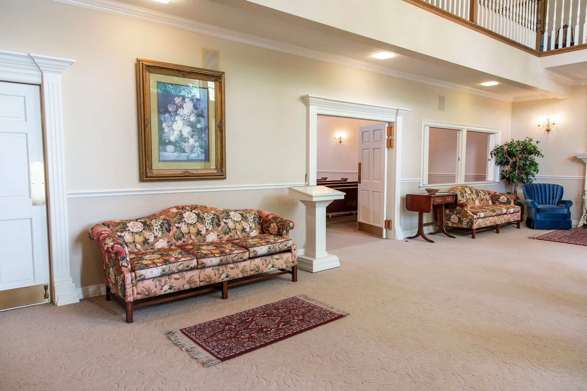 Interior of a waiting room with floral sofas, artwork, and a small rug on beige carpet.