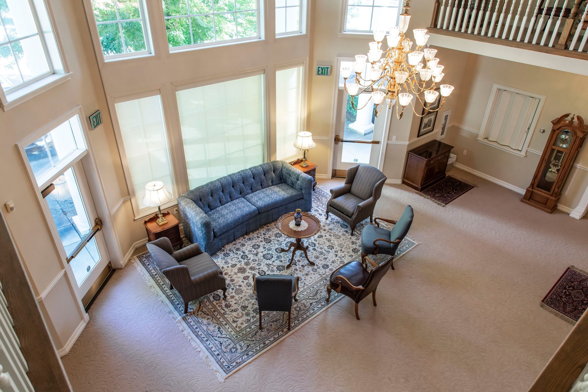 High-angle view of a lobby with seating. Blue sofa, chairs, round rug, chandelier, tall windows, and a podium.