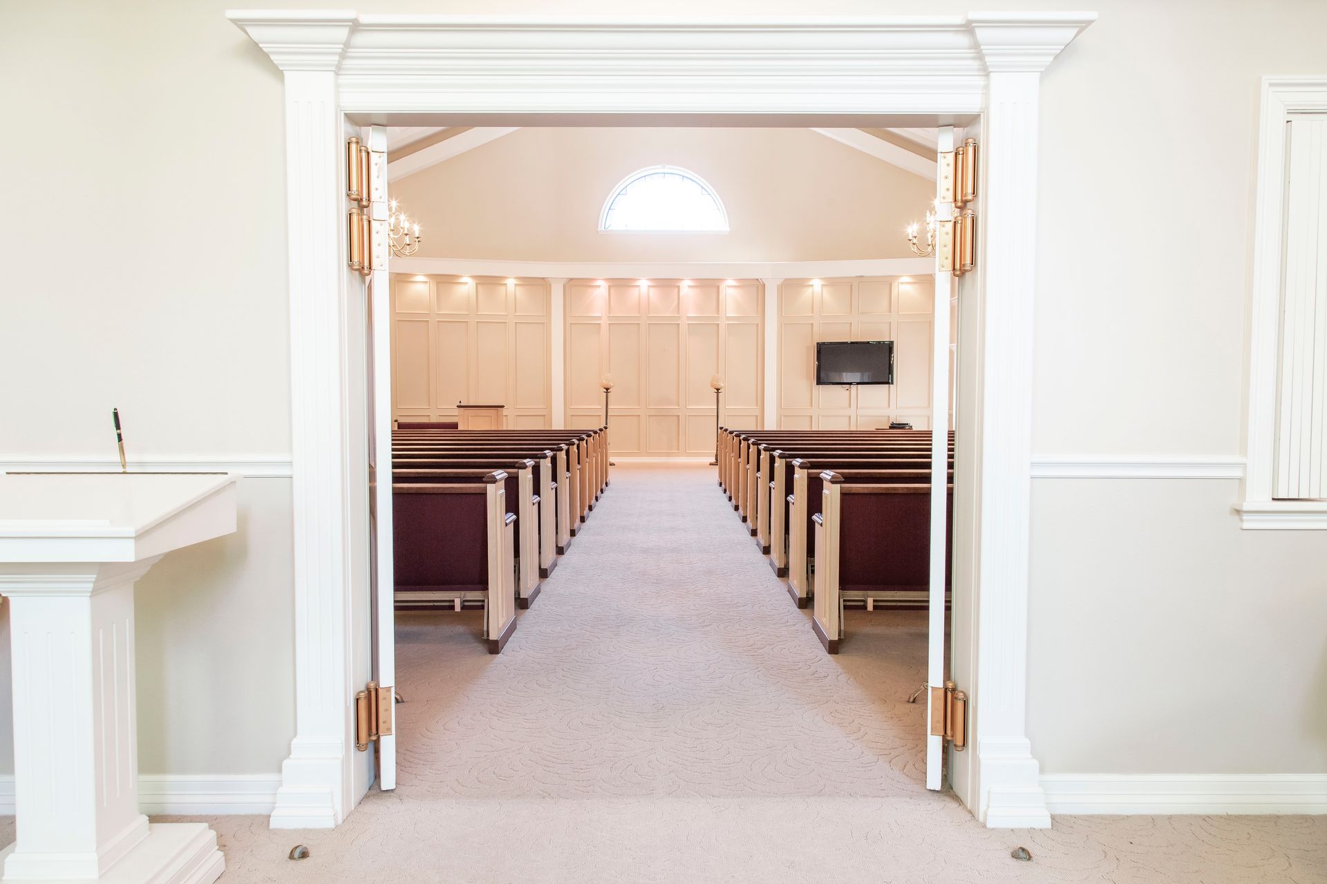 Interior of a chapel with rows of pews, a podium, and an arched window at the far end.