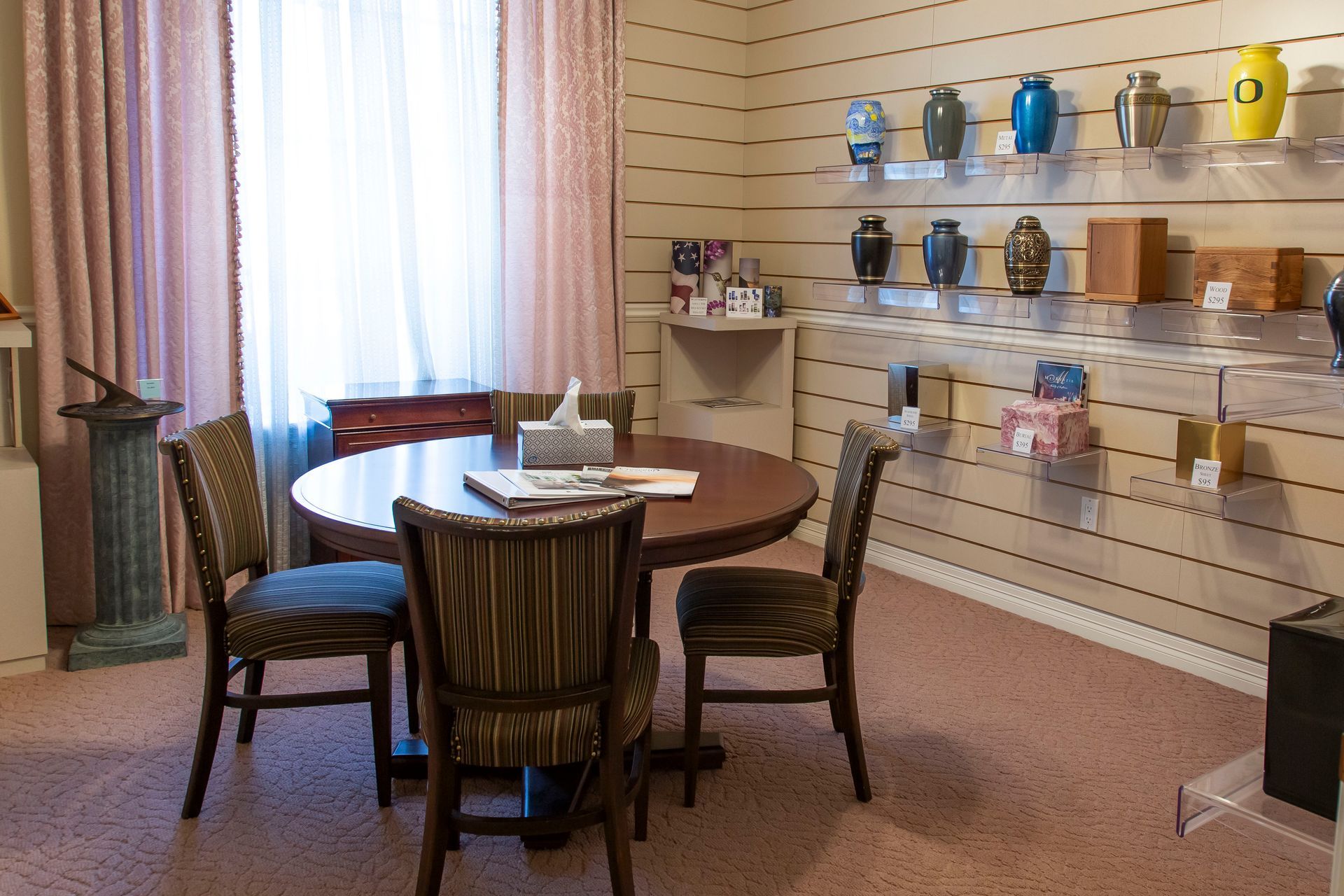 A room with a round table, chairs, window, and shelves displaying urns.