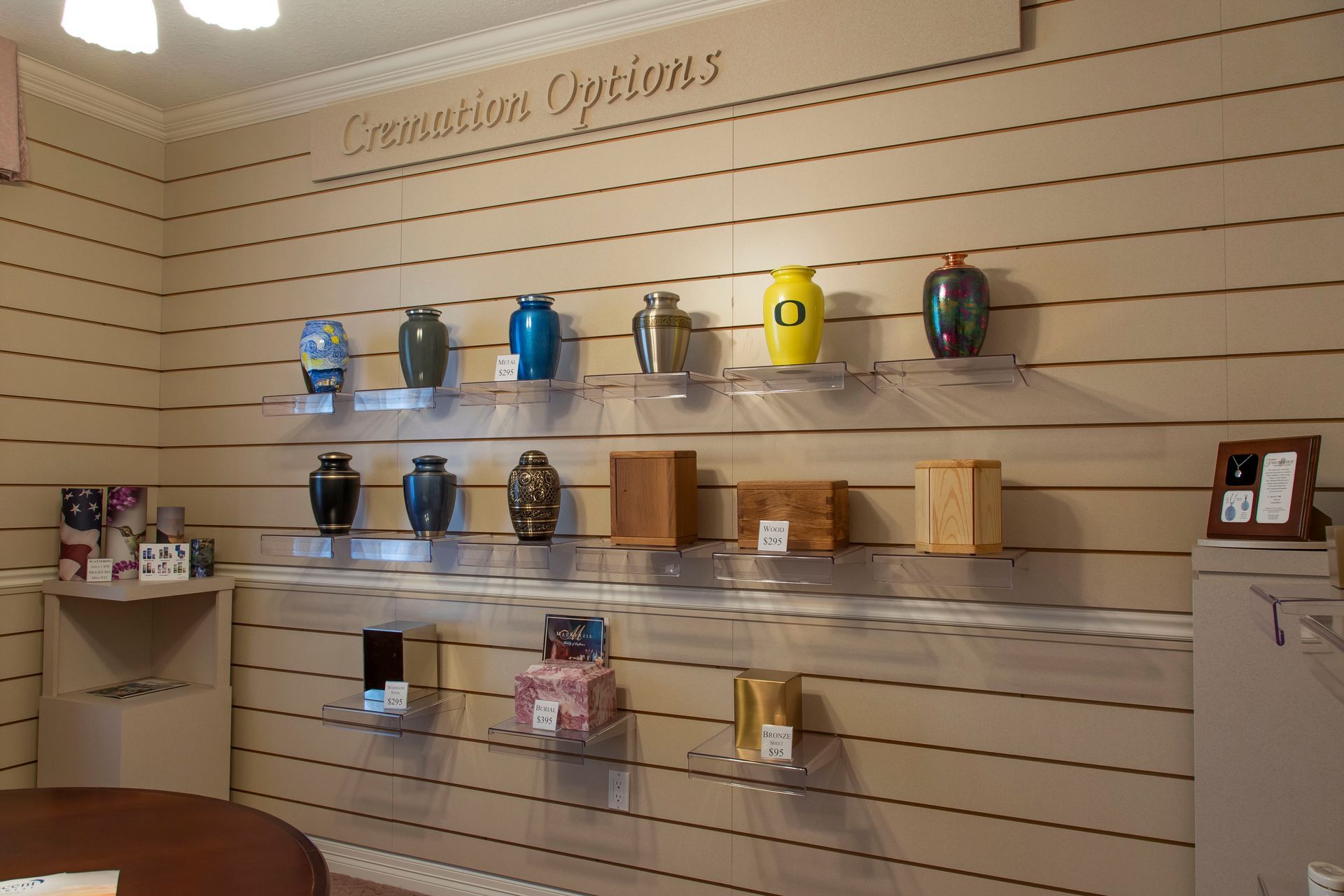 Display of cremation urns on shelves in a showroom, varying shapes, colors, and materials.