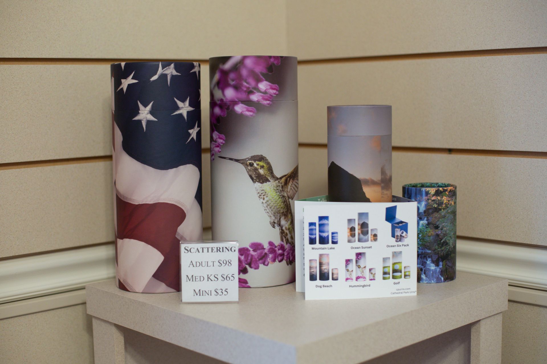 Urns on a display: American flag, hummingbird, mountain scene, floral designs.