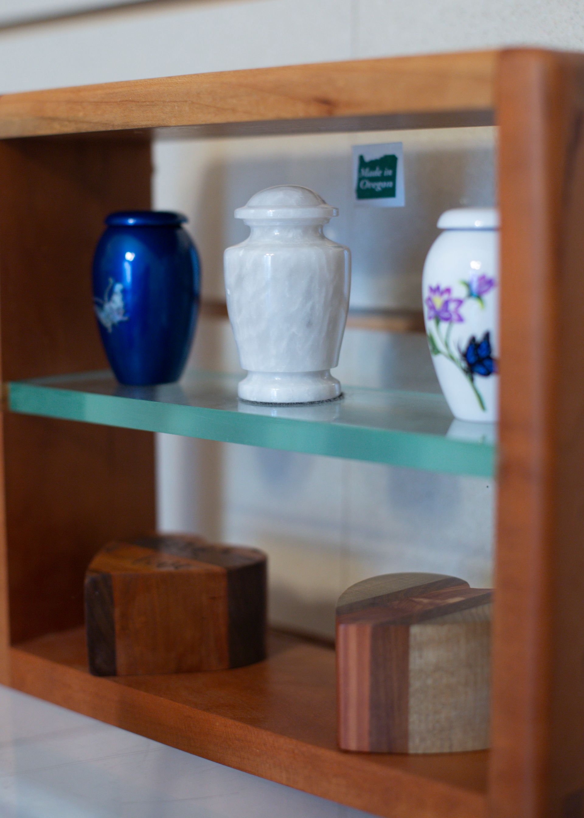 Wooden shelf with three urns: blue, marble, and floral, with wooden keepsakes below.