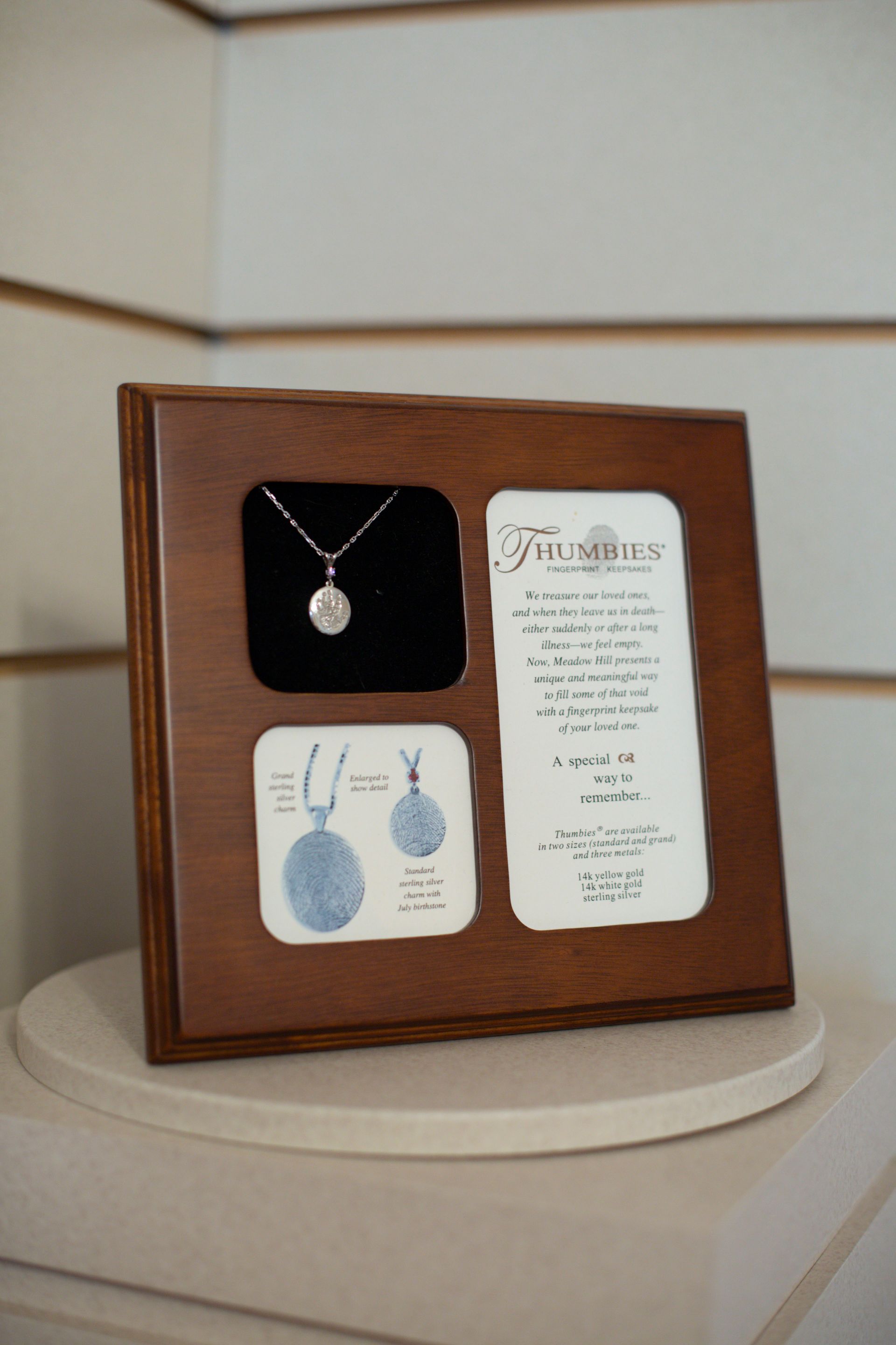 Wooden plaque with a necklace, illustration, and text on a white surface. The necklace is in a black velvet inset.