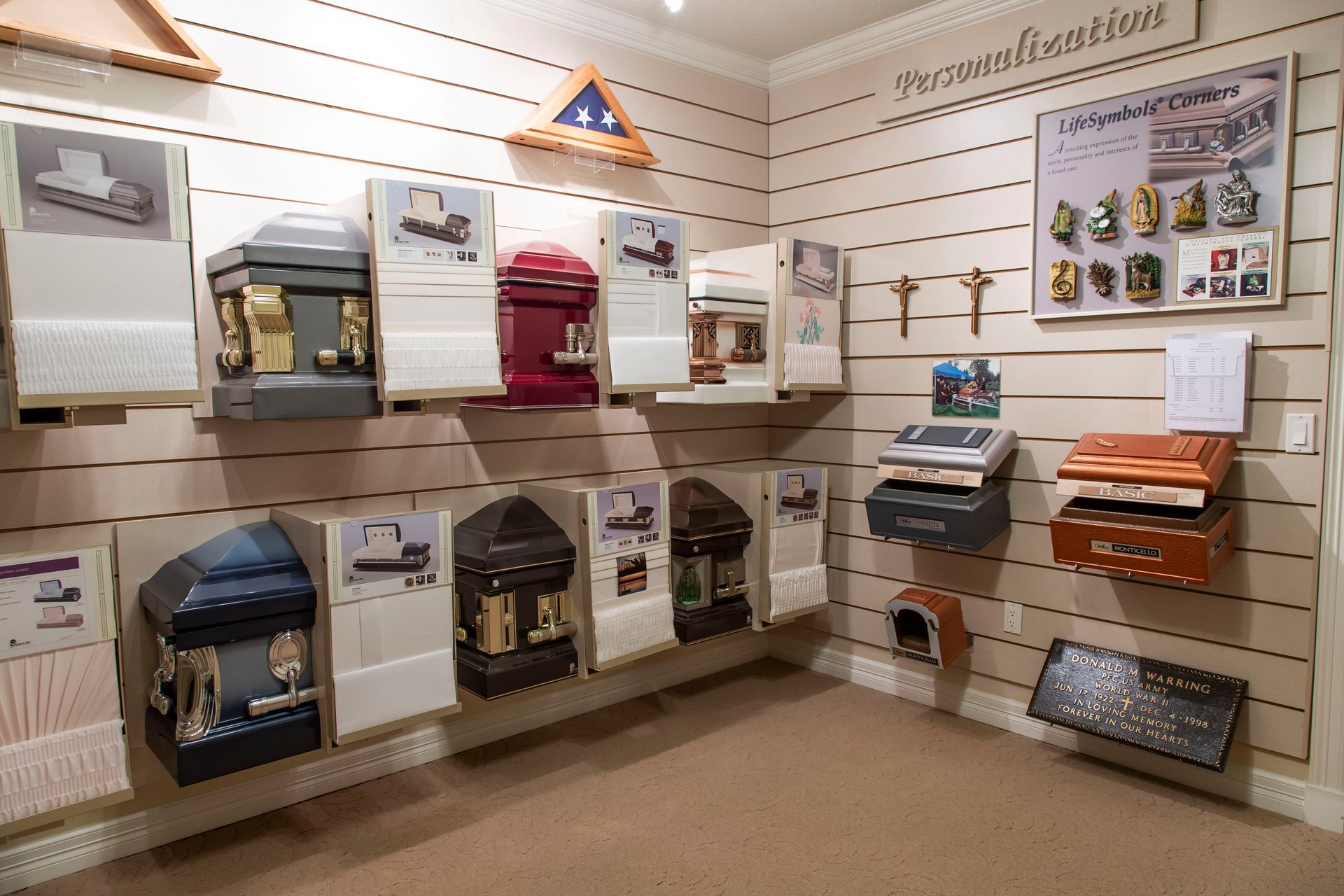 Displays of cremation urns and memorial items in a showroom, mounted on a striped wall.