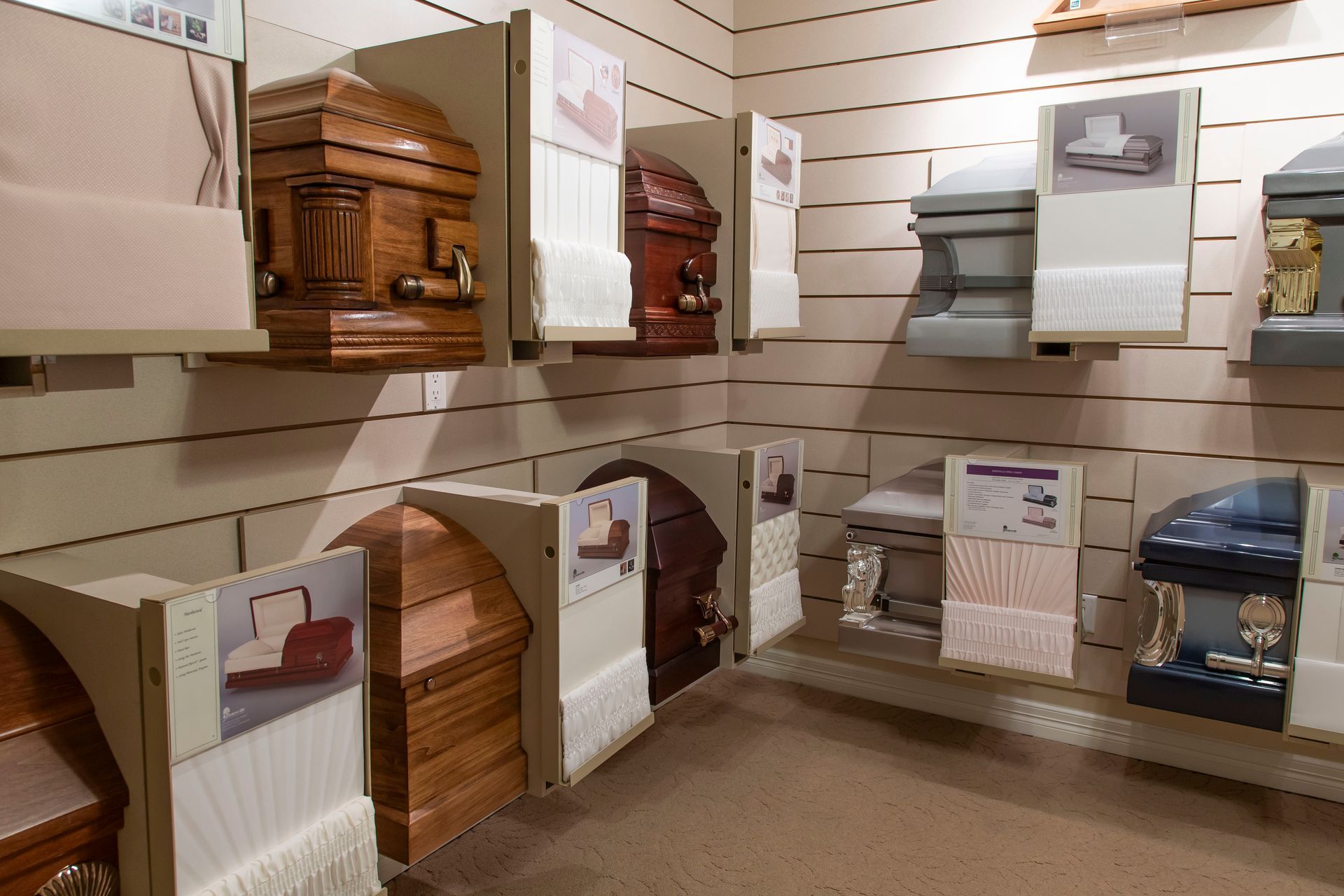 Funeral home display of caskets on shelves, various colors and styles.