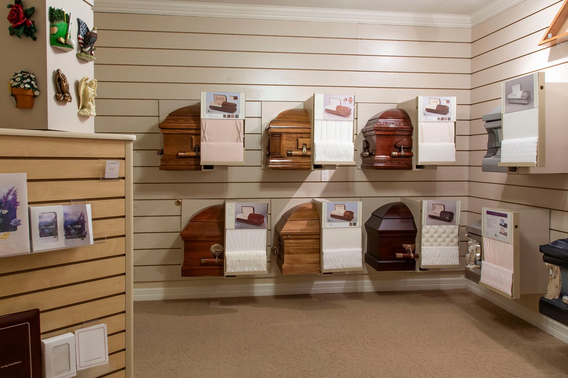 Display of caskets in a funeral home. Various styles and colors are mounted on the wall.
