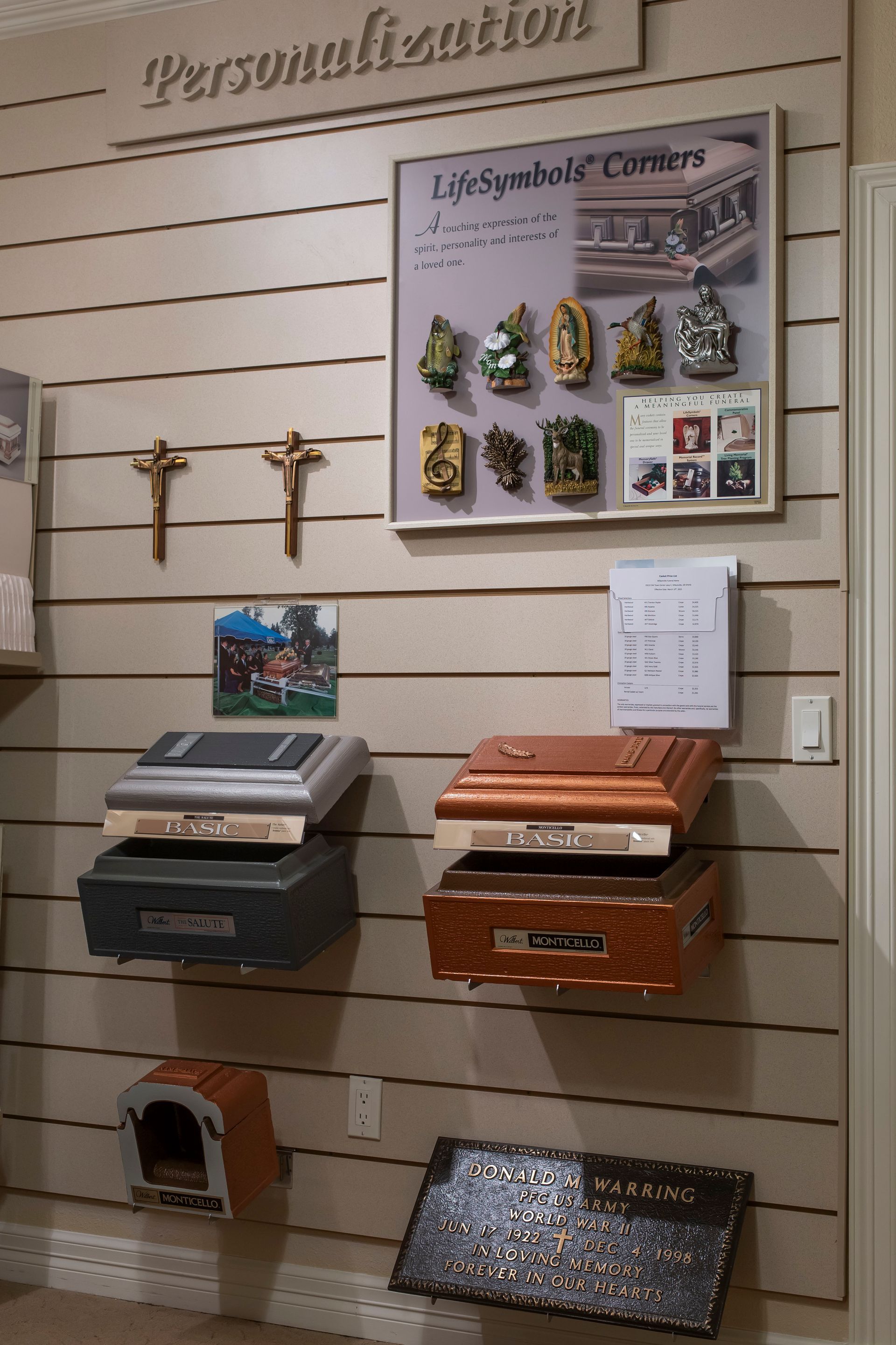 Display of urns, crucifixes, and life-symbol plaques on a wall labeled 