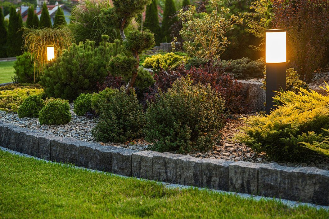 A garden with a stone wall and a lamp post in the middle of it.