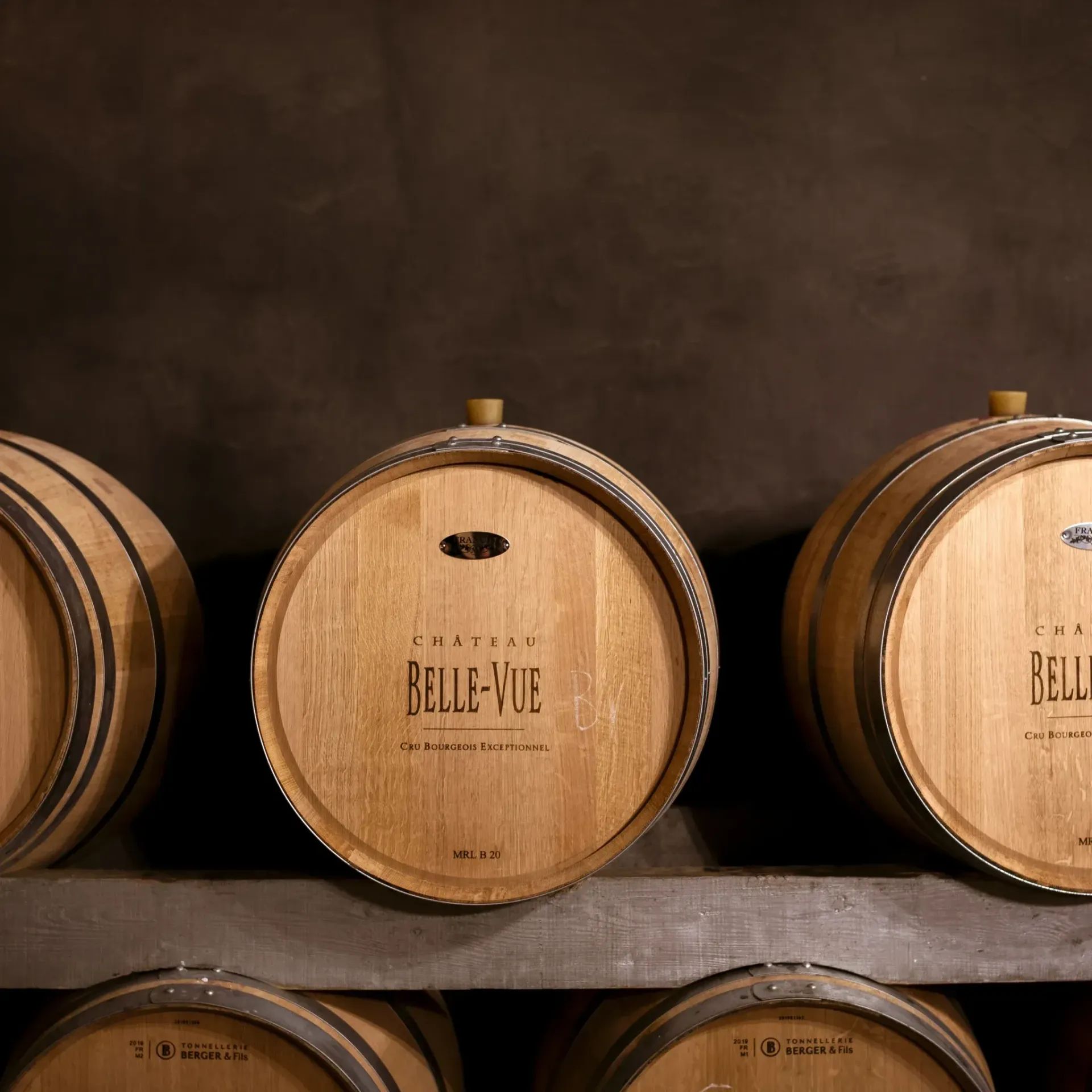 Wooden wine barrels in a dimly lit cellar, labeled 