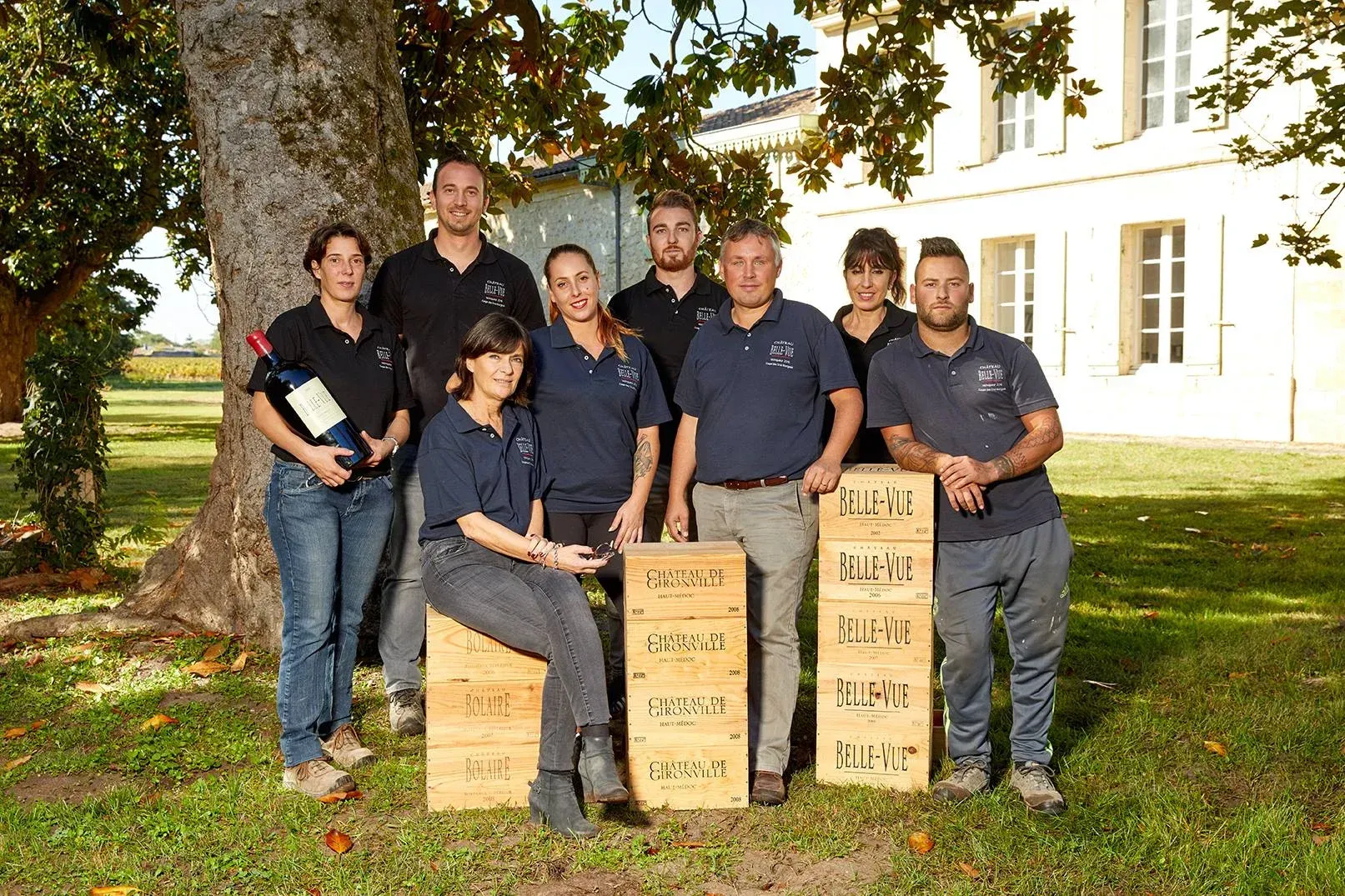 Group of people pose with wine crates outdoors, near a building, at Château Belle-Vue