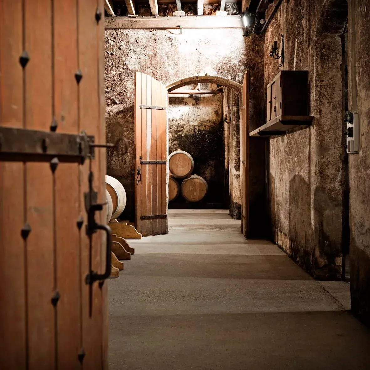 Wooden doors open into the Château Bellegrave cellar with barrels.