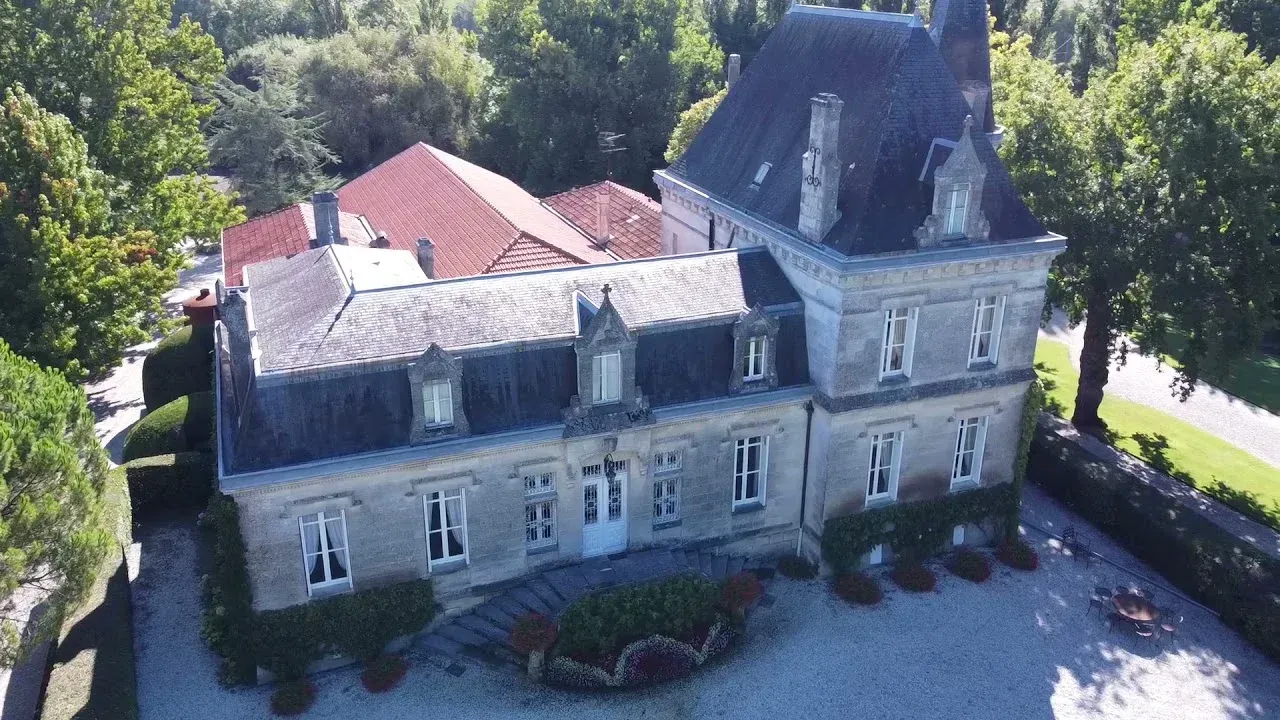Large stone building at Château Bellegrave with a slate roof, set amongst trees, with a driveway.