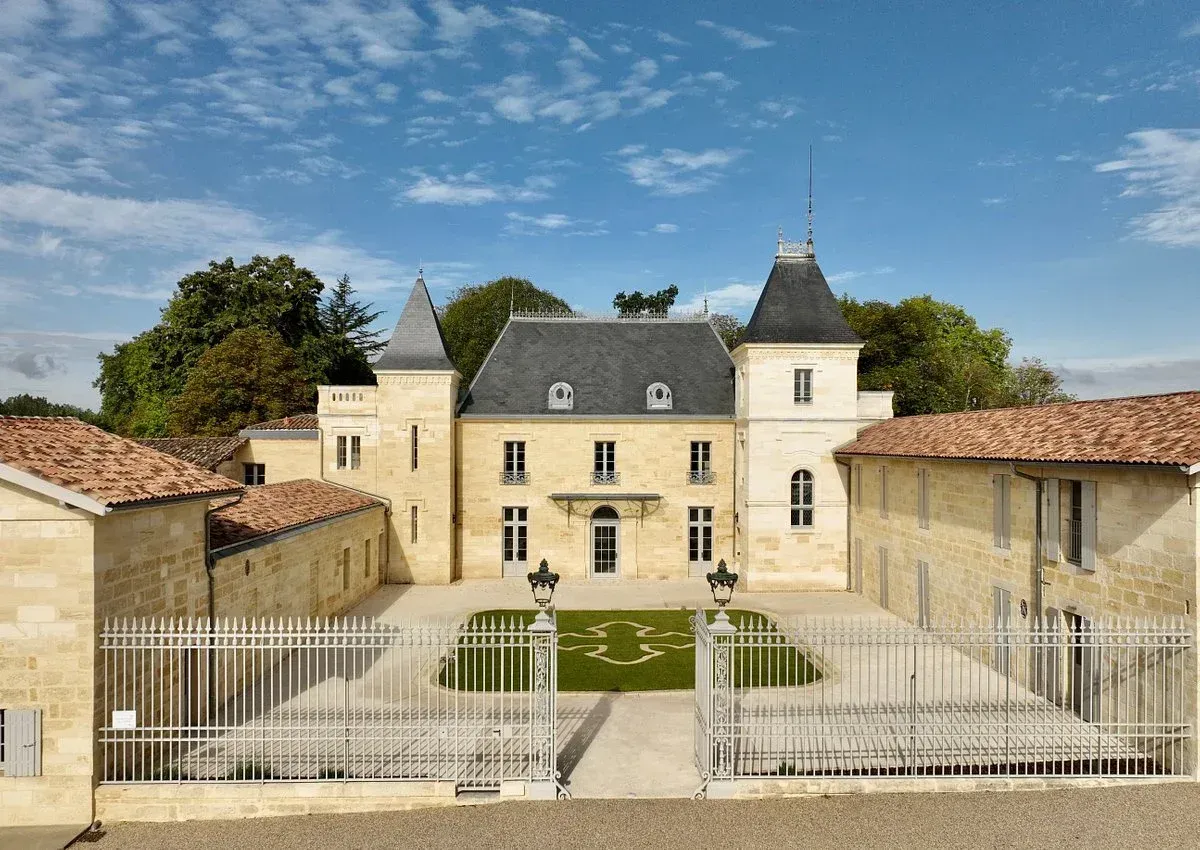 Château with light yellow facade, gray roof, and surrounding walls, under a blue sky.