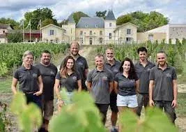 Group of people standing in front of Château de Chambrun vineyard, and a building in the background.