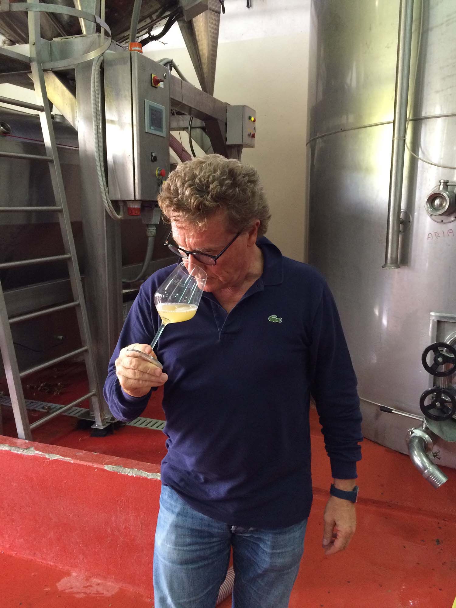 Paolo Controneo in blue shirt smelling wine in a glass, industrial setting with tanks and equipment.