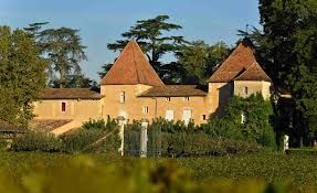 Building with two prominent reddish-brown conical towers, surrounded by trees and a vineyard, at Château Carbonnieux