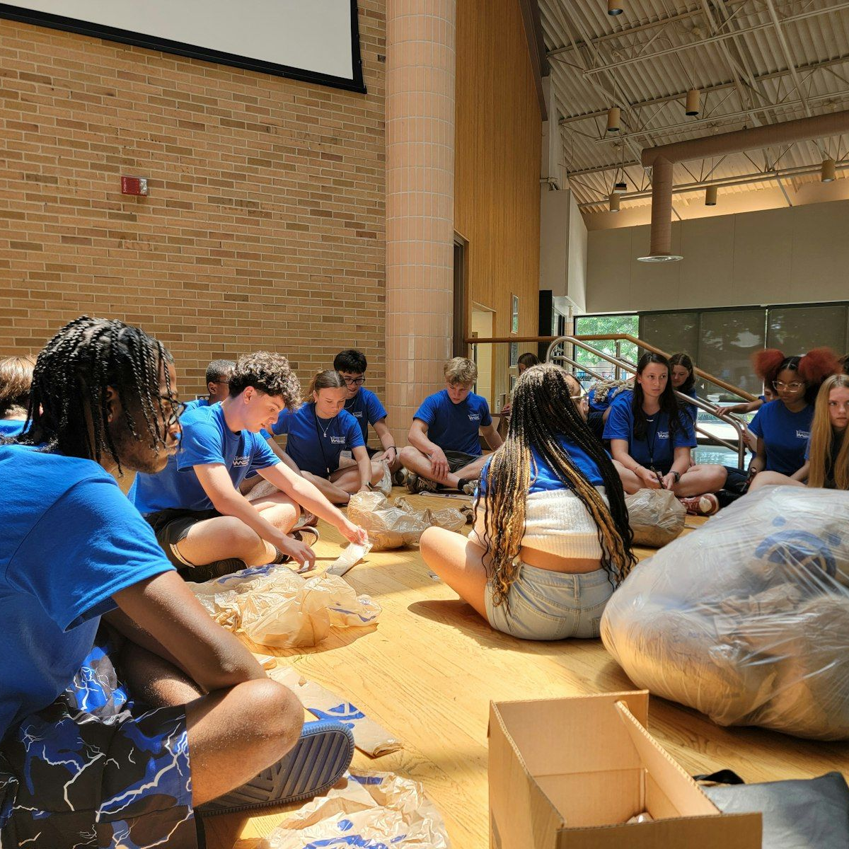 Girl with brown hair, smiling, wearing a hairnet, gloves, and a green shirt, leaning on a table.