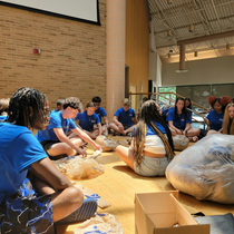 Girl with brown hair, smiling, wearing a hairnet, gloves, and a green shirt, leaning on a table.