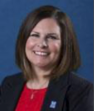 A professional headshot of a smiling person wearing a red top and black blazer against a solid blue background.