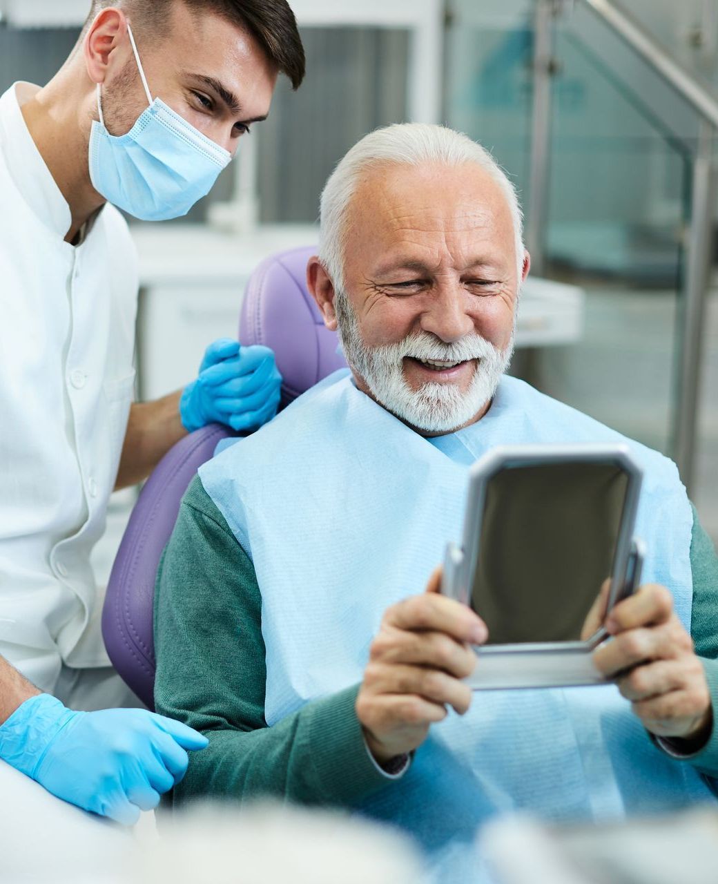 Get dental implants, dentures, veneers, and more at our top dental practice in Garland TX 75040 RESTORATIVE DENTISTRY | old man smiling in mirror at dental office | Veneers, implants, dentures