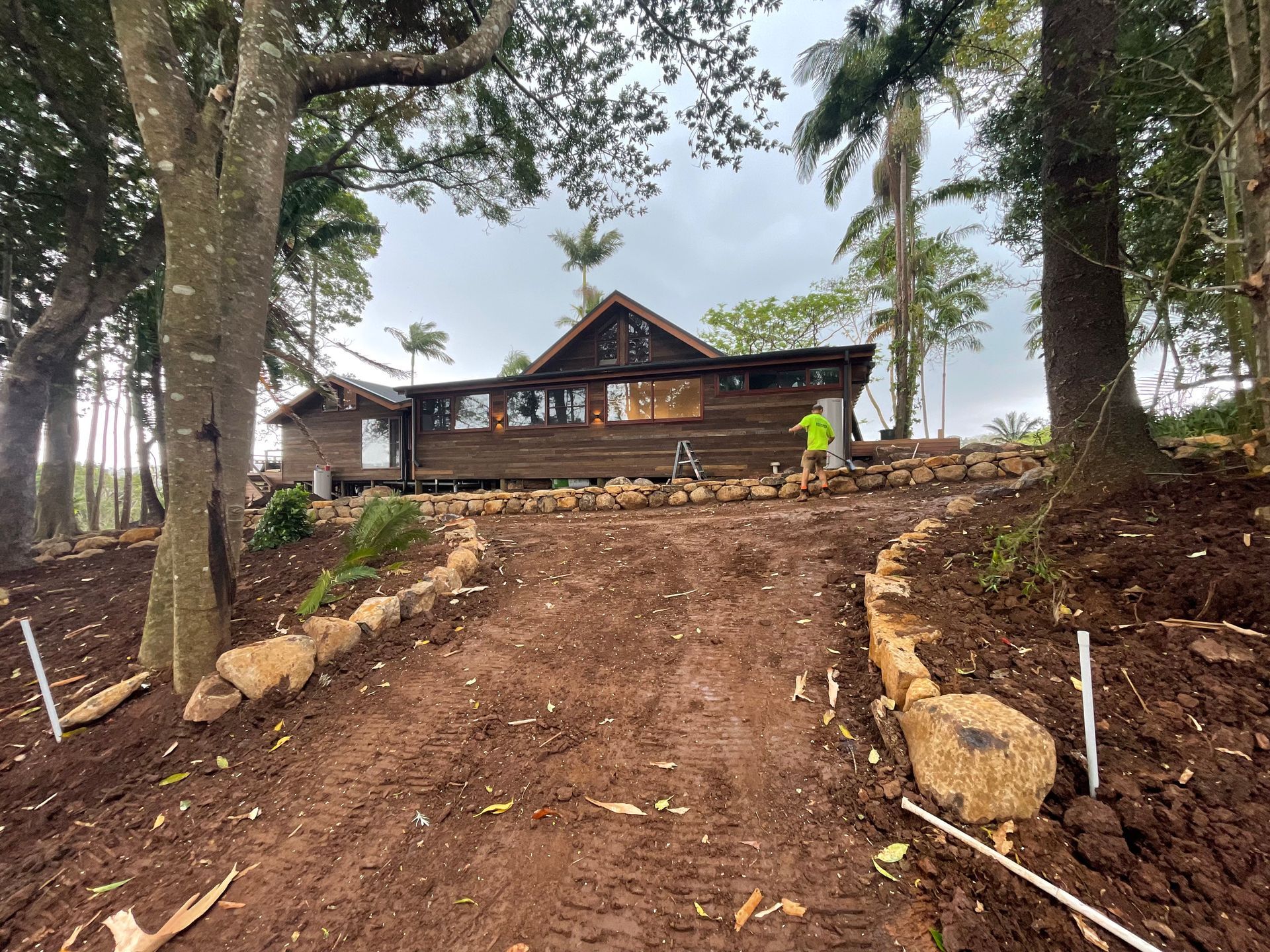 A Man Is Working On A Driveway Next To A House — East Point Earthmoving in Byron Bay, NSW