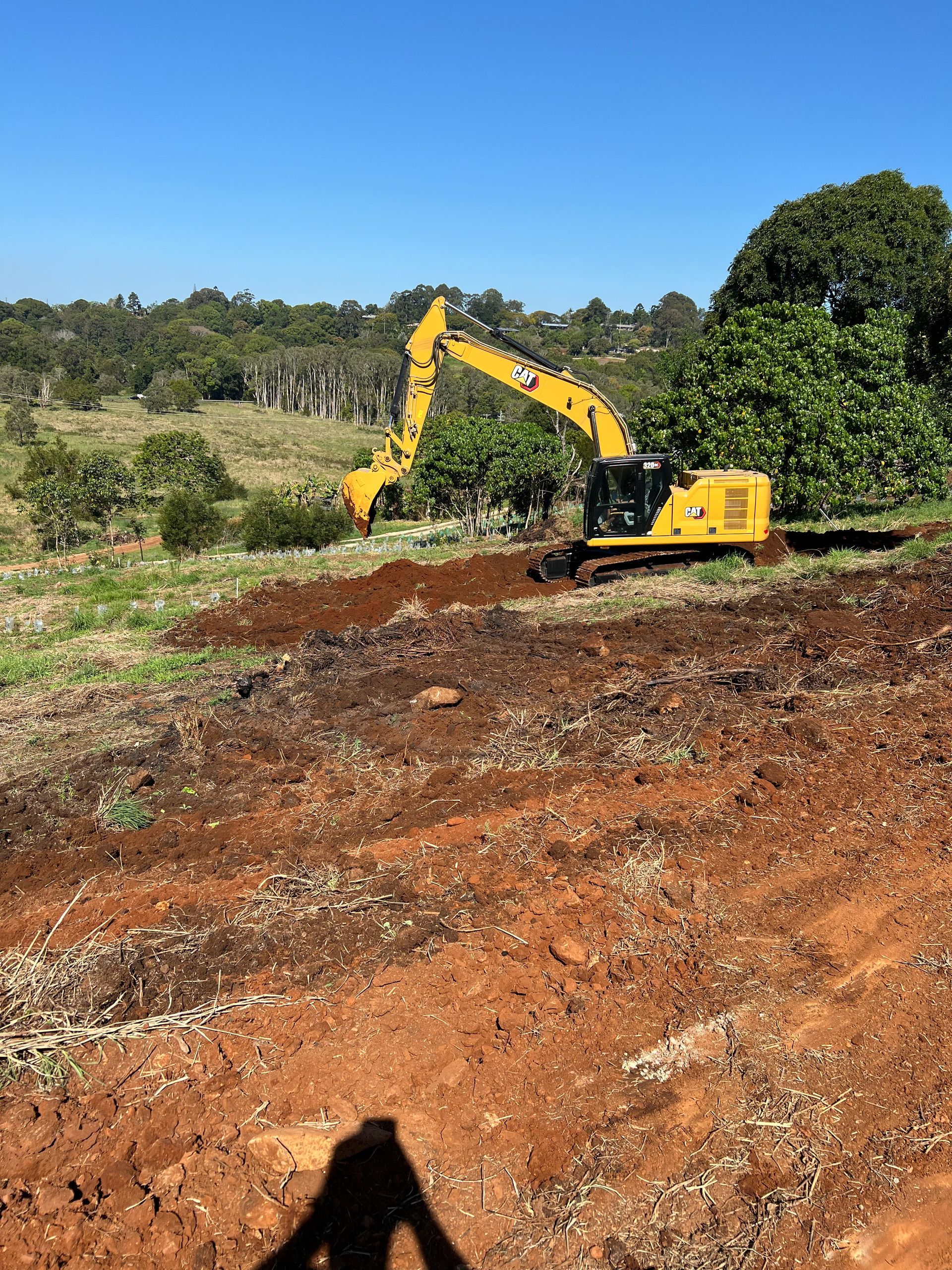 A Yellow Excavator Is Digging A Hole In A Field — East Point Earthmoving in Byron Bay, NSW