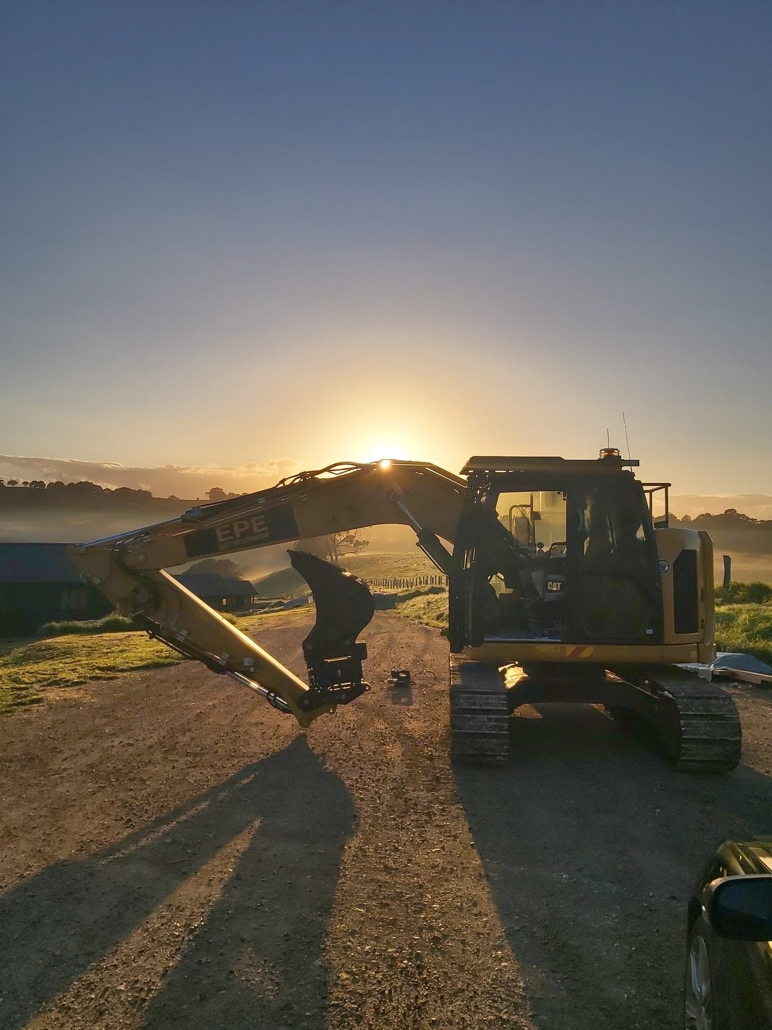 A Digger Is Sitting On Asphalt In The Sunset — East Point Earthmoving in Byron Bay, NSW