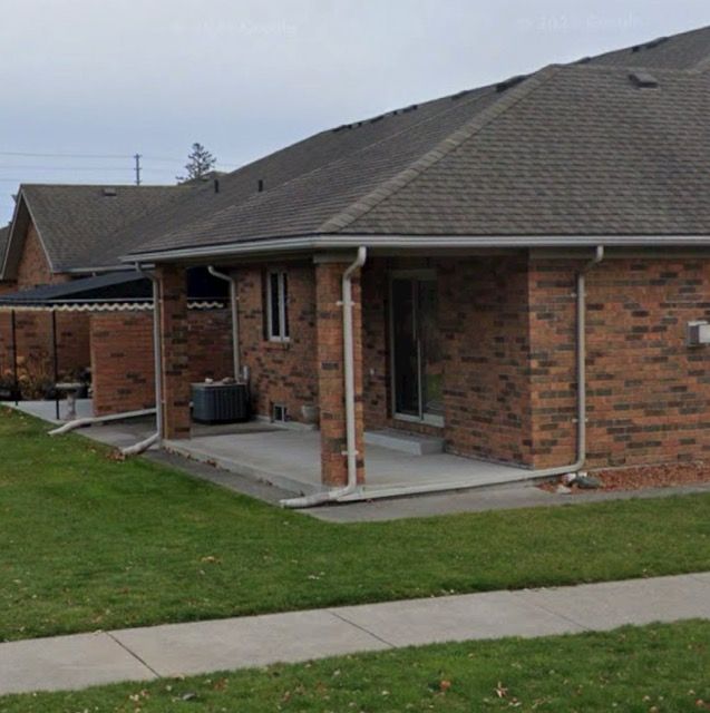 A rear view of brick residential townhouses featuring covered patios, sliding glass doors, and white downspouts.