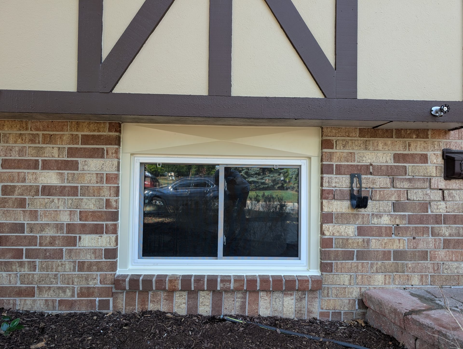 A white-framed sliding window installed in a tan brick wall beneath a timber-framed overhang.