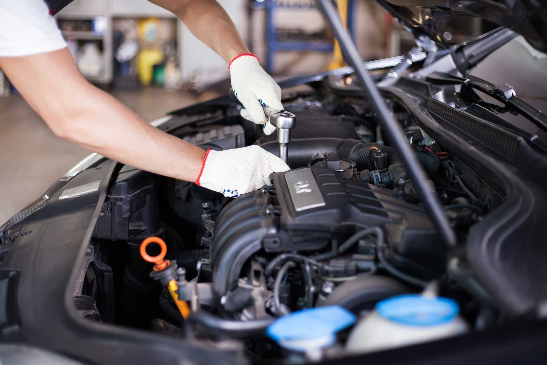 Mechanic with gloves working on a car engine in a parking garage. He is using a wrench, focused on the task.