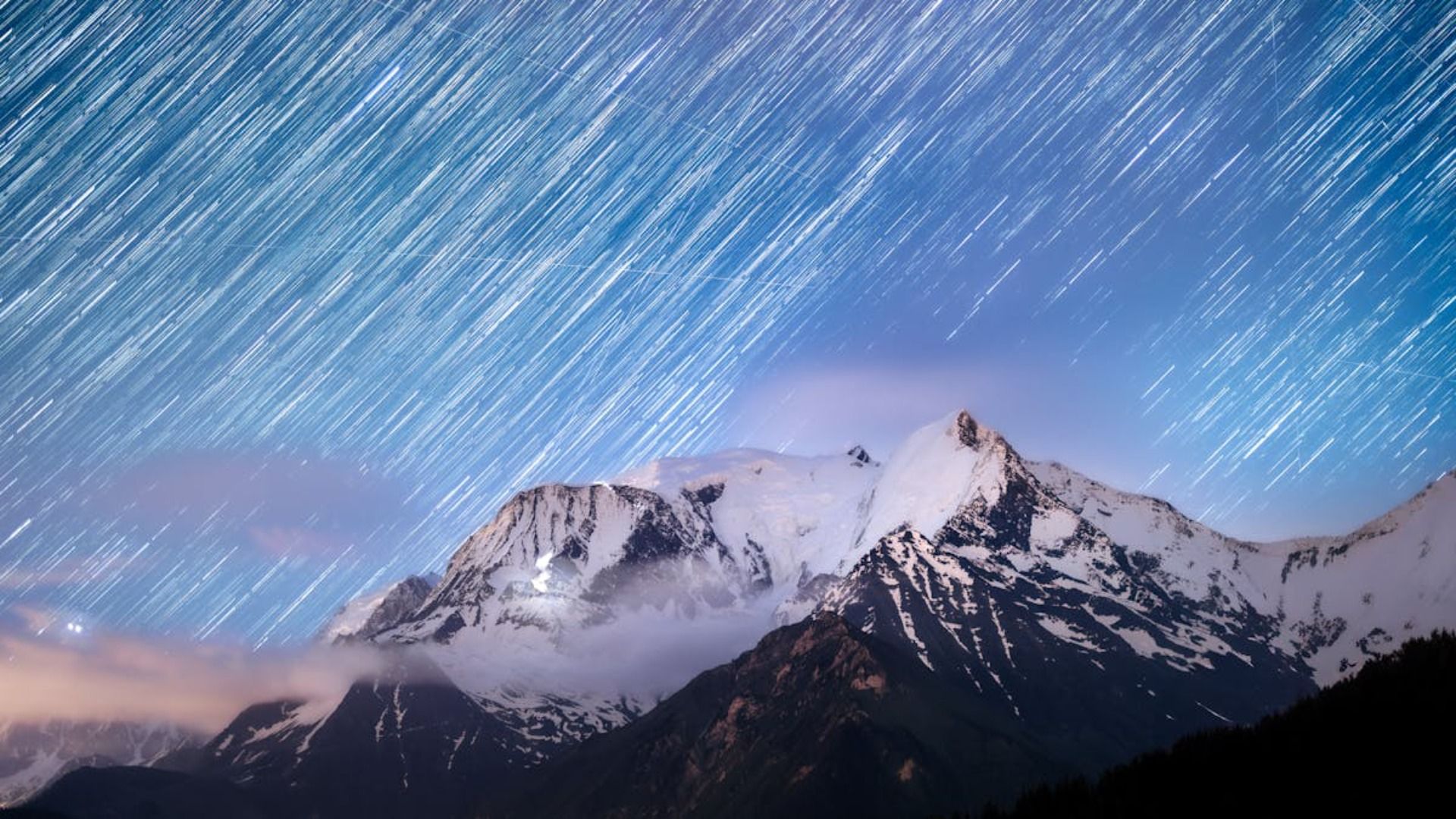 Cordillera nevada bajo un cielo estrellado con rayos de luz.