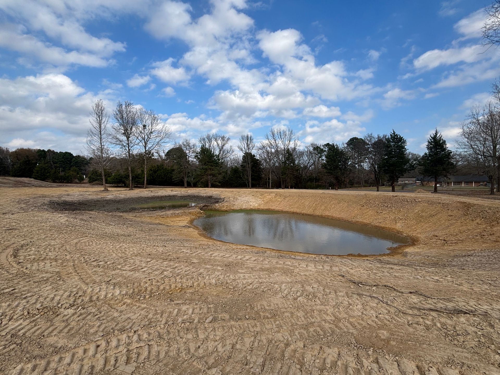 Yellow excavator loading dirt into a yellow dump truck near a body of water.