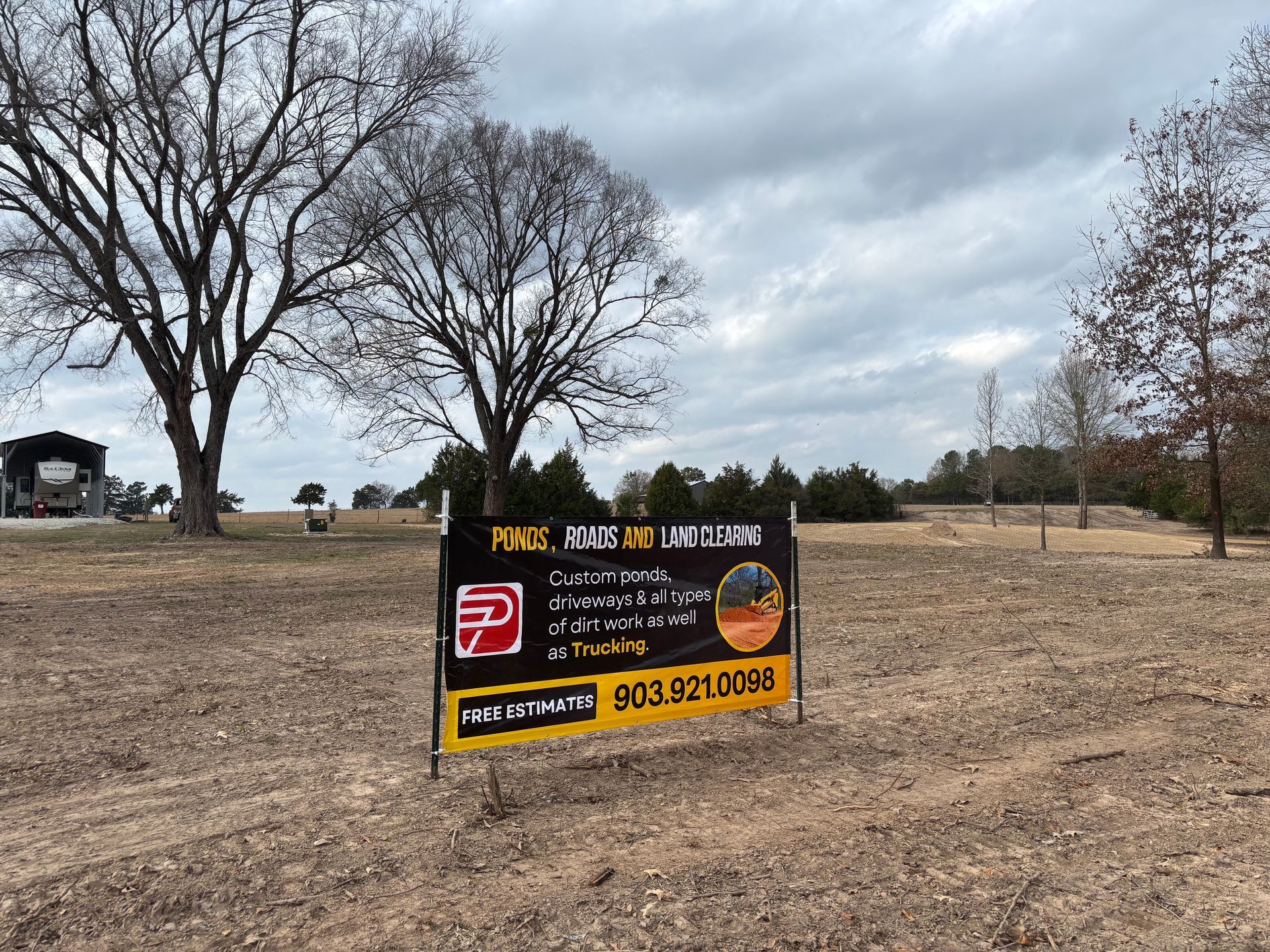 Gravel driveway through a grassy area, leading towards a treeline on a cloudy day.