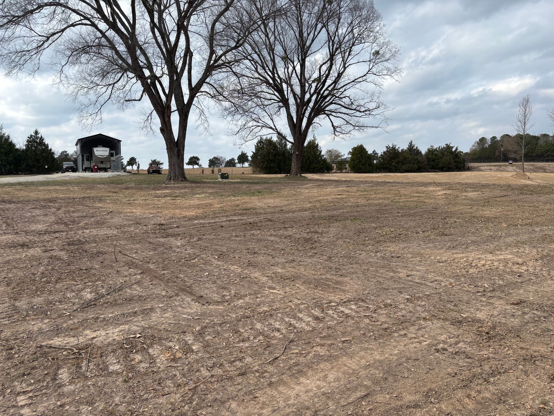Gravel driveway through a grassy area, leading towards a treeline on a cloudy day.