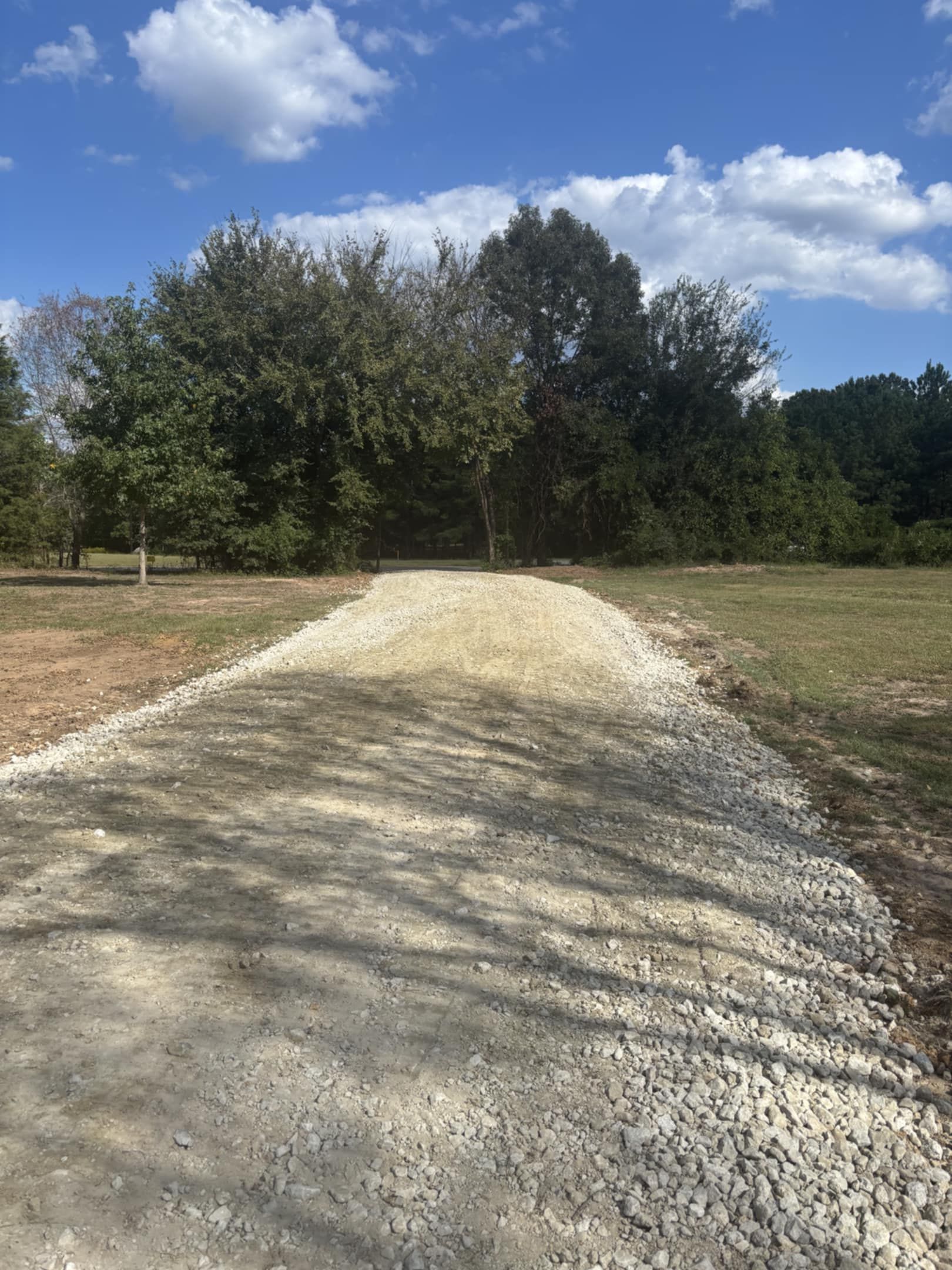 Garage with a gravel driveway and carport on a sunny day. Brown and gray siding.