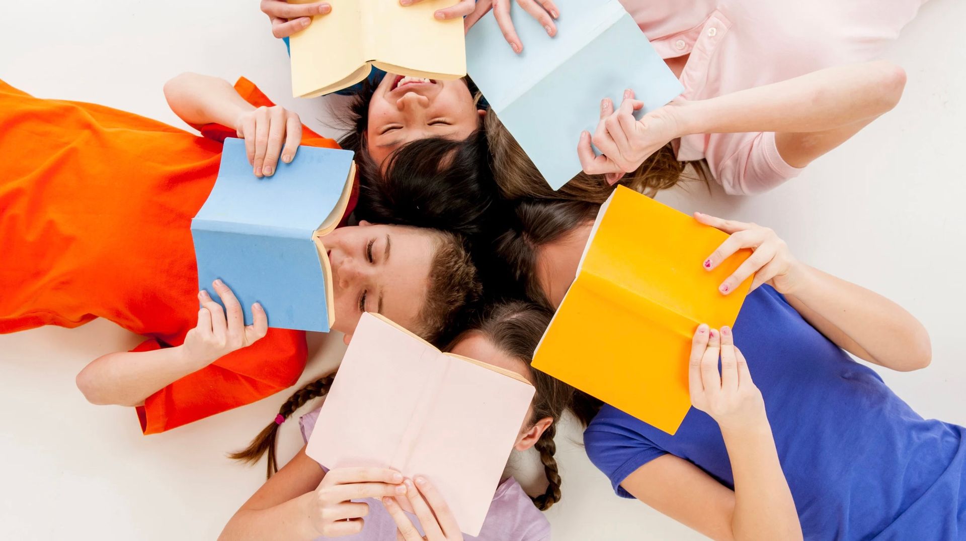 A group of diverse kids lying in a circle, reading books with colorful covers.