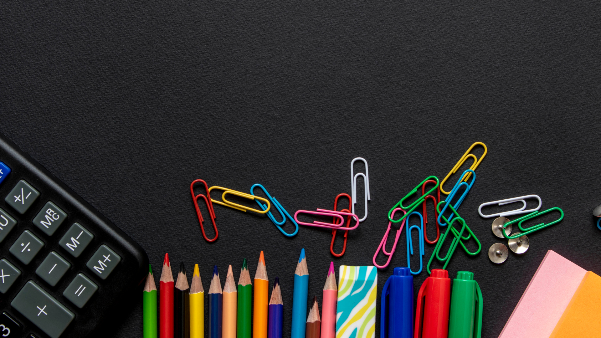 A calculator , pencils , paper clips , pens and sticky notes on a black table.