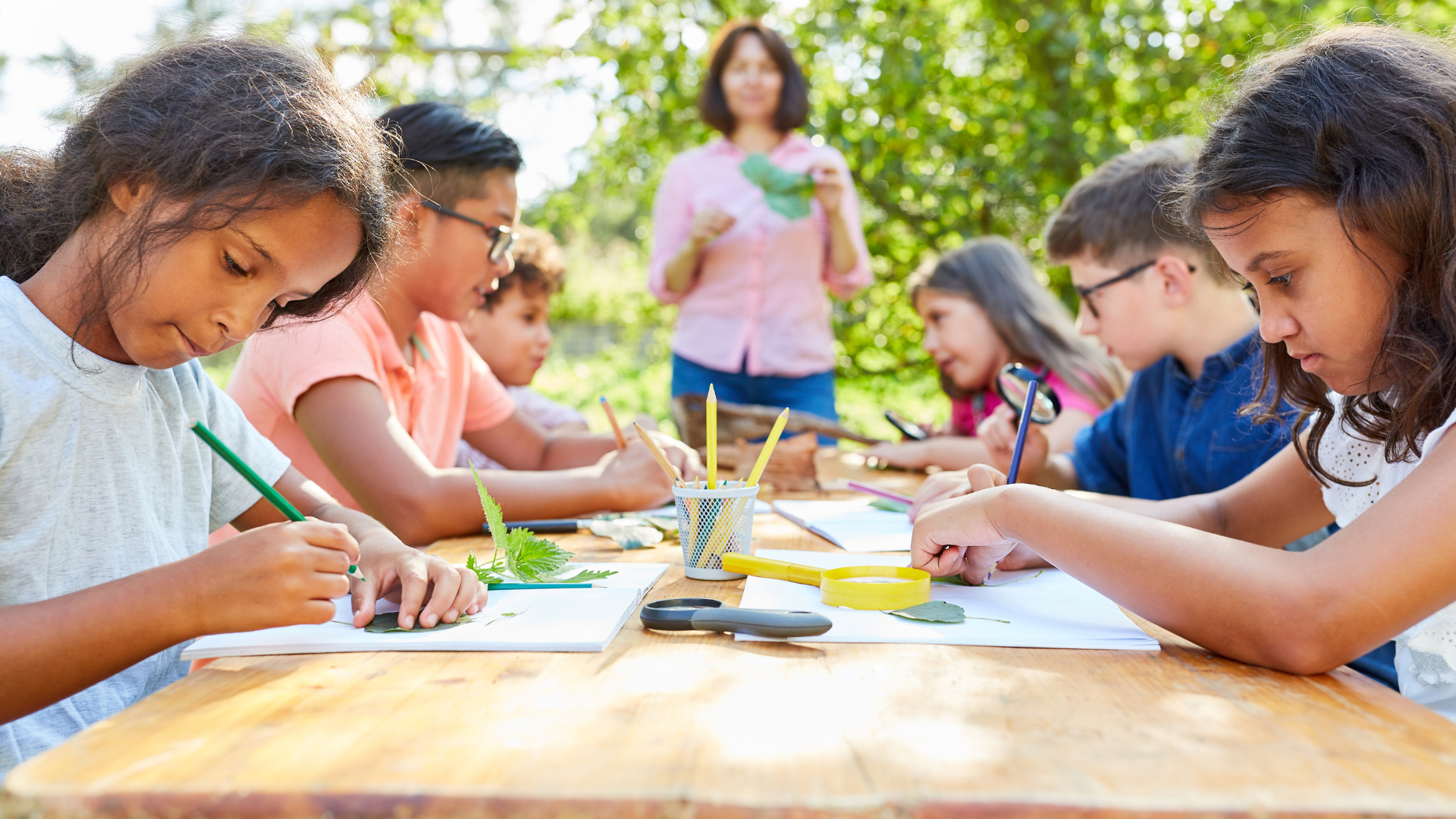 A group of children are sitting at a table with their teacher.