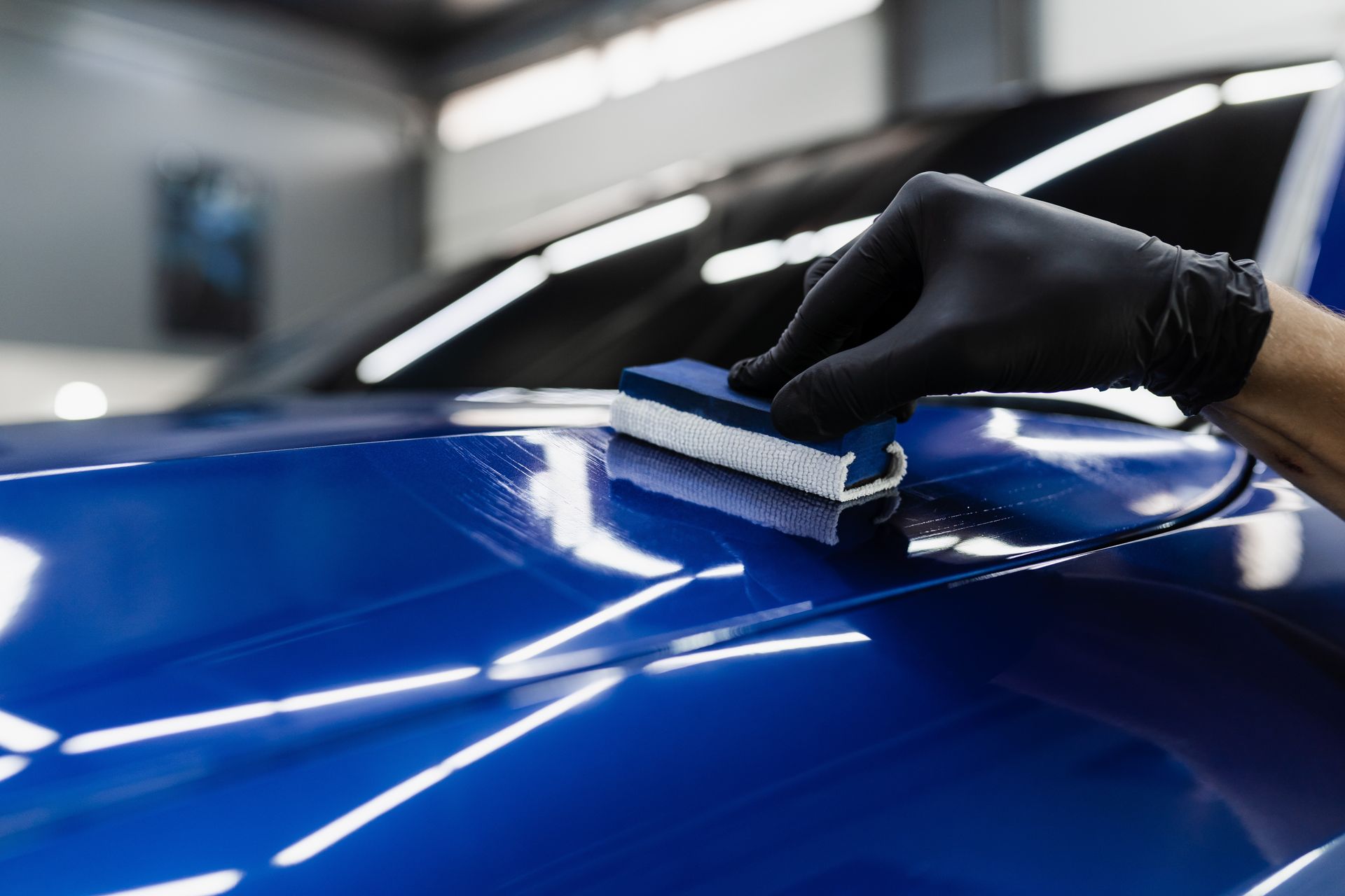 Gloved hand polishing a blue car hood in a garage