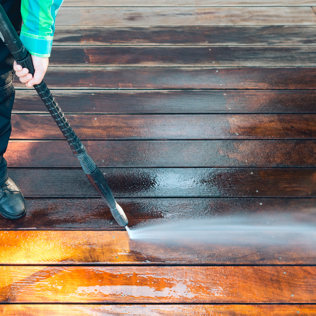 A person is using a high pressure washer to clean a wooden deck.