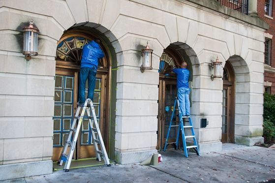 A man is vacuuming the floor and a woman is cleaning the windows.