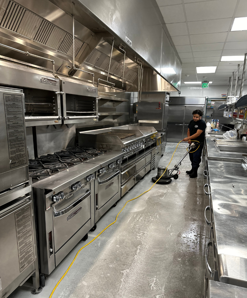 A man is performing a deep kitchen cleaning with a floor power washer.